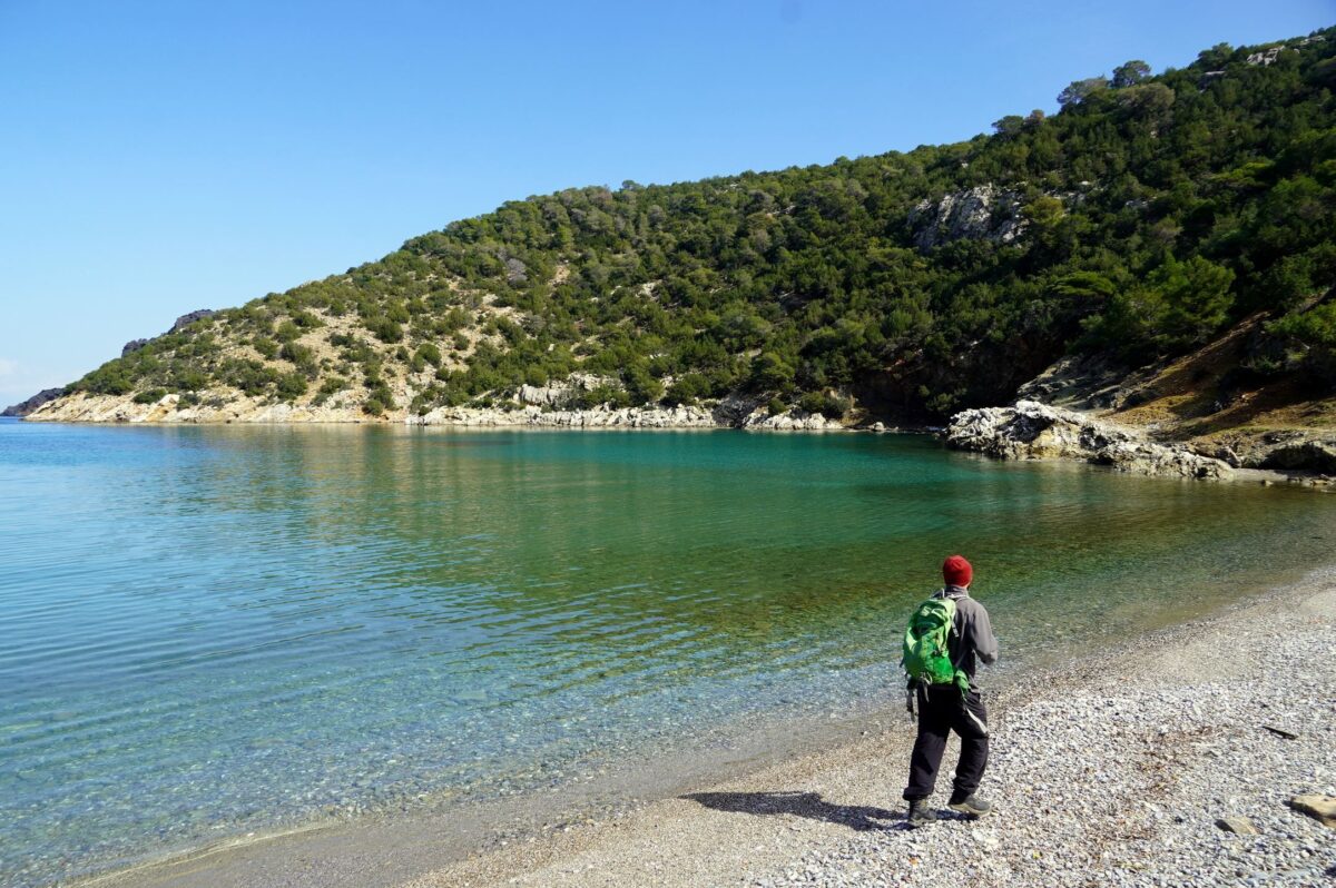 A hiker on a beach on Poros, part of the Poros Trails network