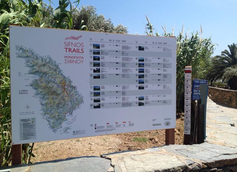 A board with a map figuring the Sifnos Trails network next to a directional hiking pole