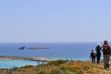 People hiking on a Kythera Trail toward Diakofti bay, with sea at the background and a shipwreck