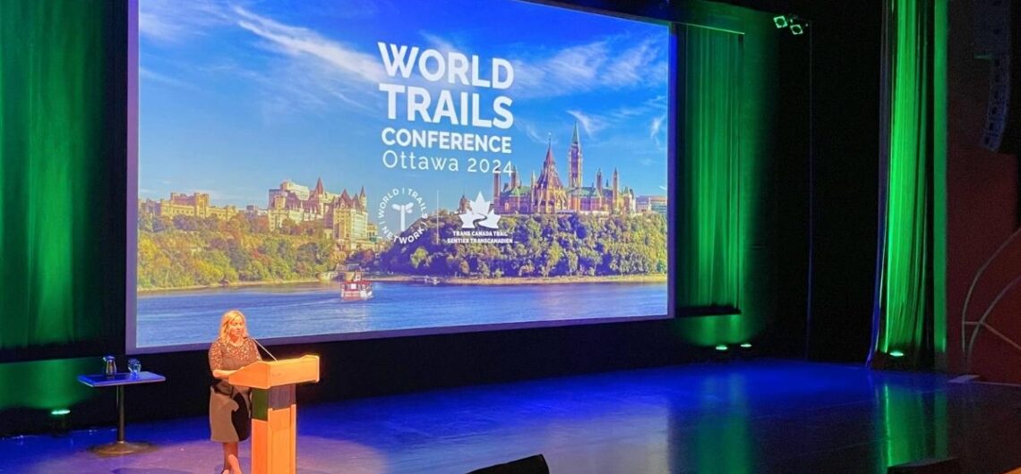 A person speaking at the World Trails Conference with a large presentation screen at the background