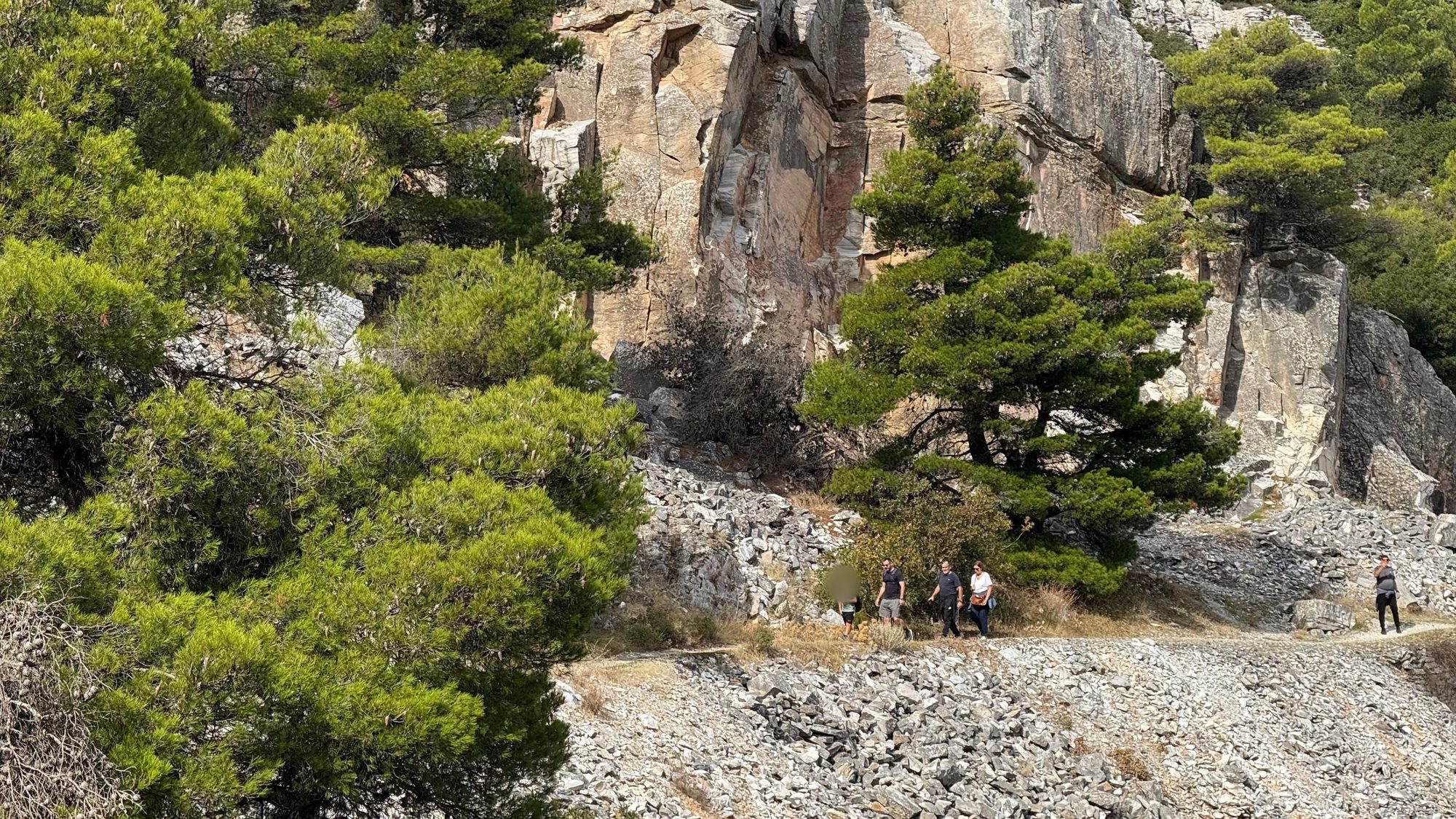 Hikers walking beneath the rock faces of the old marble quarry on trail D1 on Mount Penteli